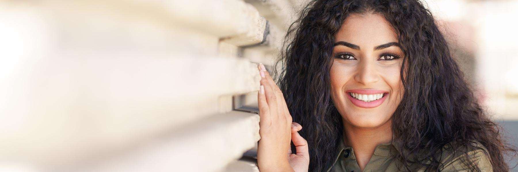 A smiling woman leaning on a fence | dentist on Kingsway