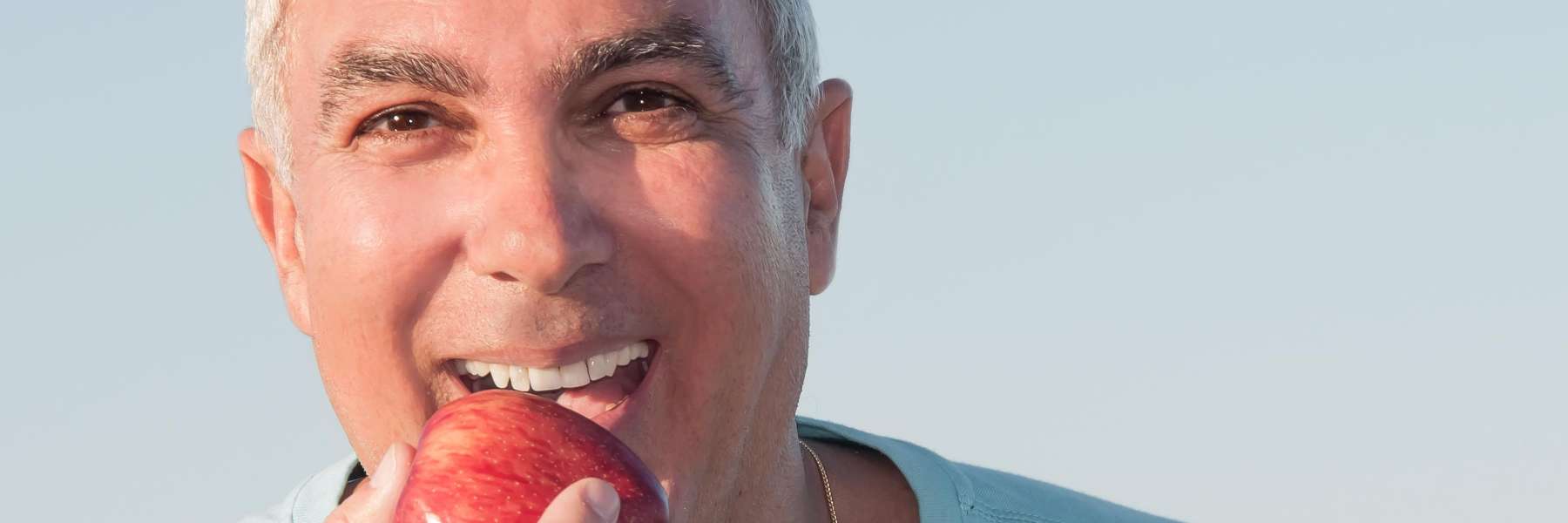 A smiling man eating an apple | Vancouver dentist