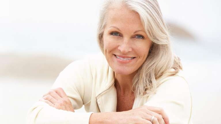 A woman smiling on the beach | overdentures in Vancouver