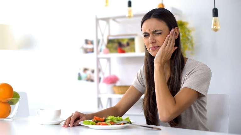 A woman with jaw pain eating a salad