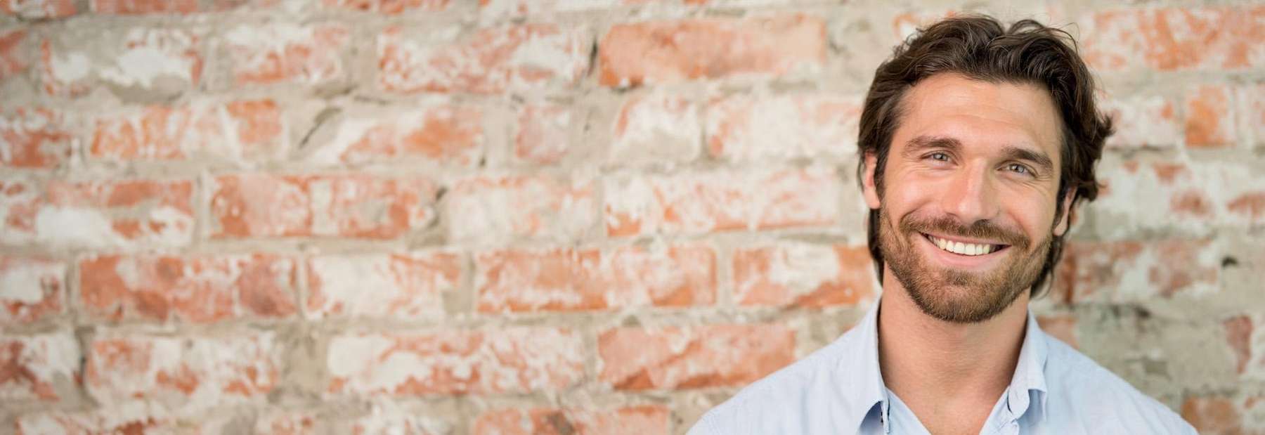 A man smiling against a brick wall | teeth whitening vancouver